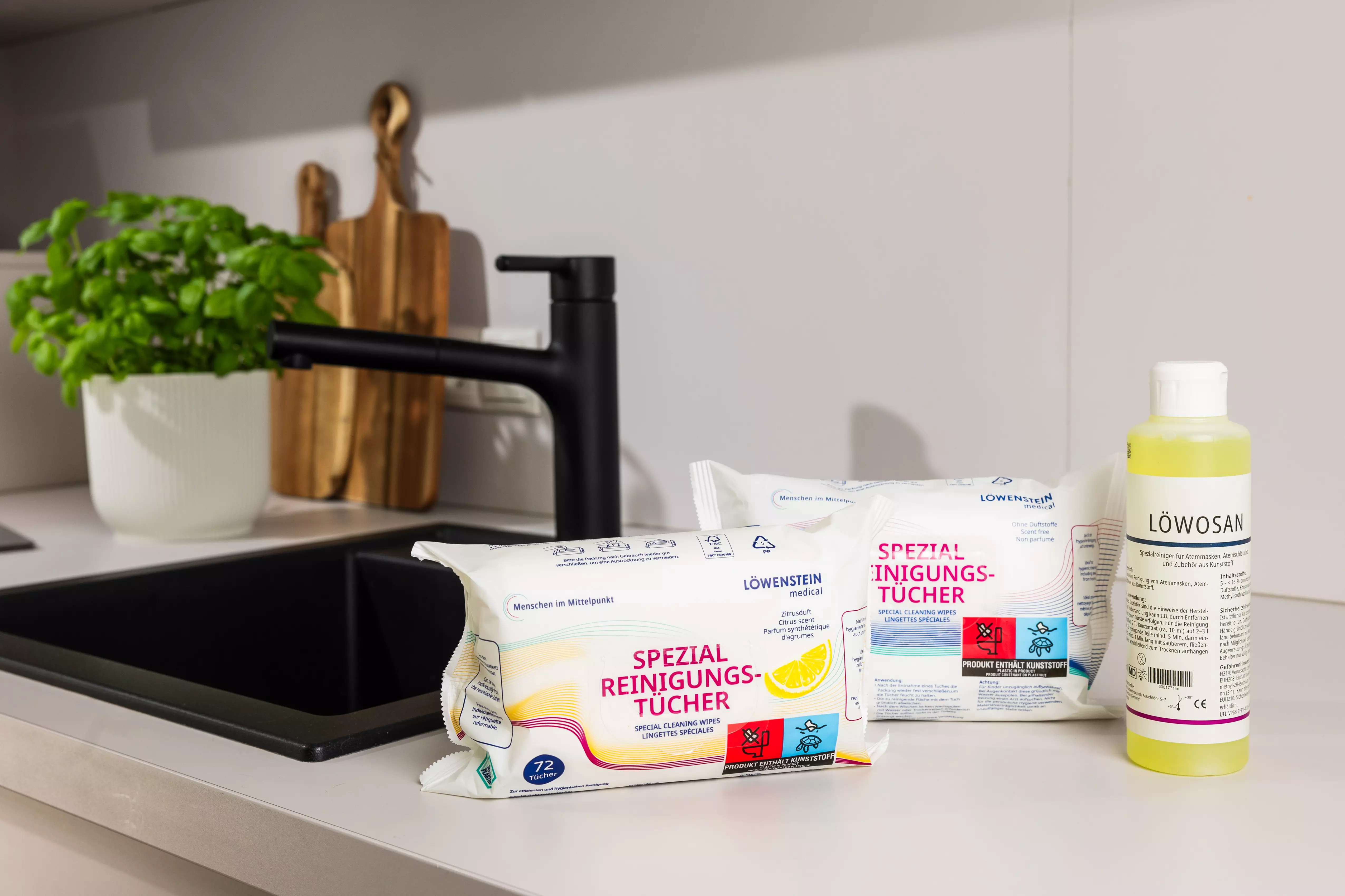 Zwei Päckchen Reinigungstücher mit neutralem und Zitronengeruch stehen zusammen mit dem Löwosan Reiniger auf einer Küchenoberfläche. 